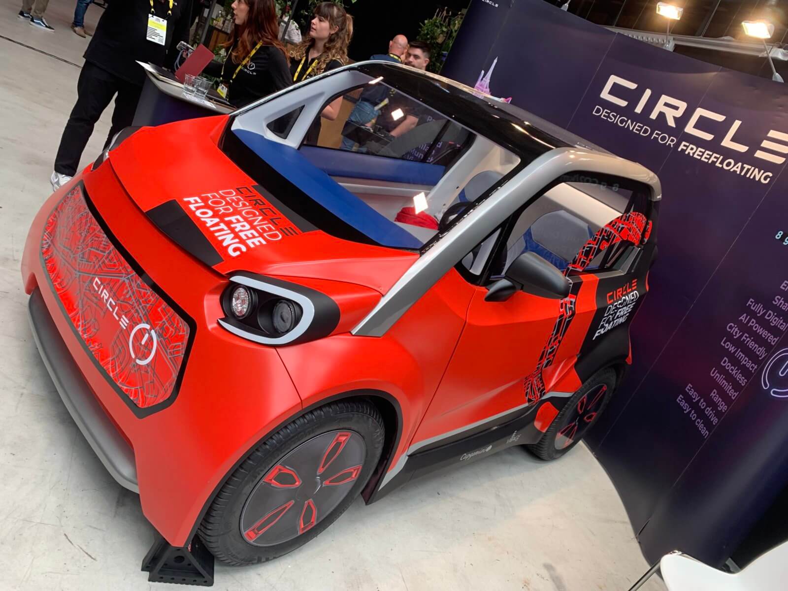 A vibrant red and black Circle electric city car on display, with text 'Designed for Freefloating' across the hood, featuring a modern design with stylized graphics, at an automotive exhibition.